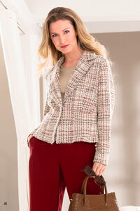 "Een blonde vrouw met een rode broek, een beige blazer met een licht rood ruitjespatroon en een handtas in haar hand."